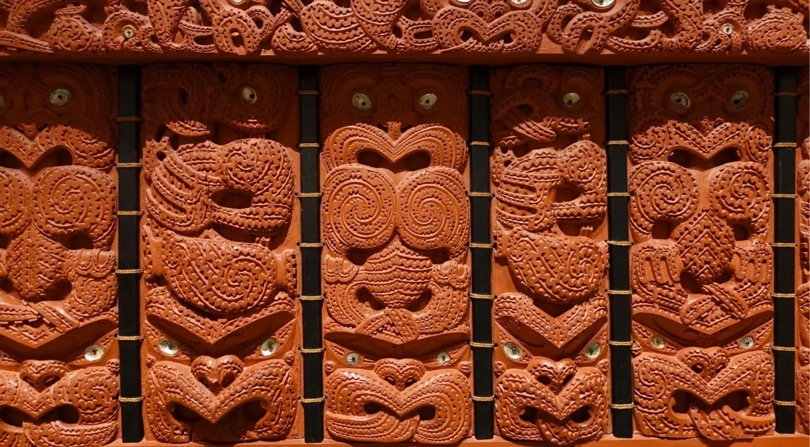 Interior wall of carved poupou ancestor panels with pāua shell eyes, bound with black and gold lashings