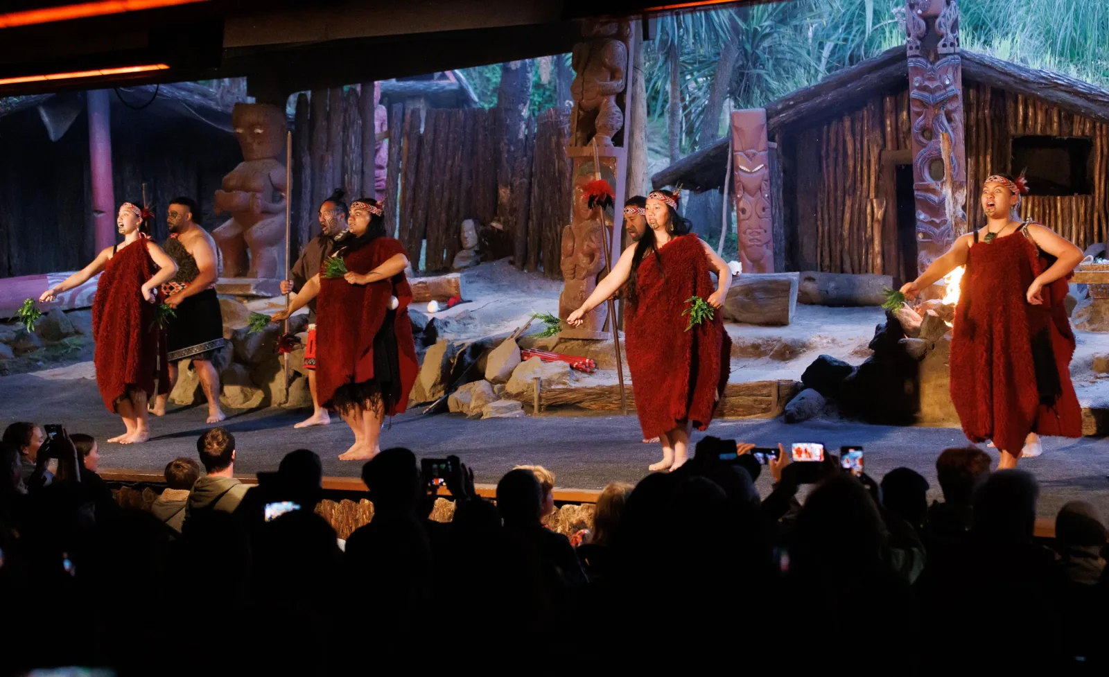 Mitai performers in red korowai cloaks on stage in the evening, with the audience watching from the dark