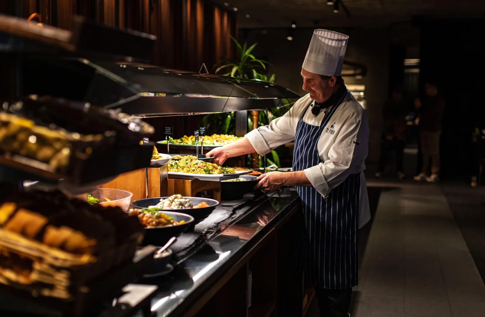 A chef in a Te Puia apron serving at the Pātaka Kai buffet counter