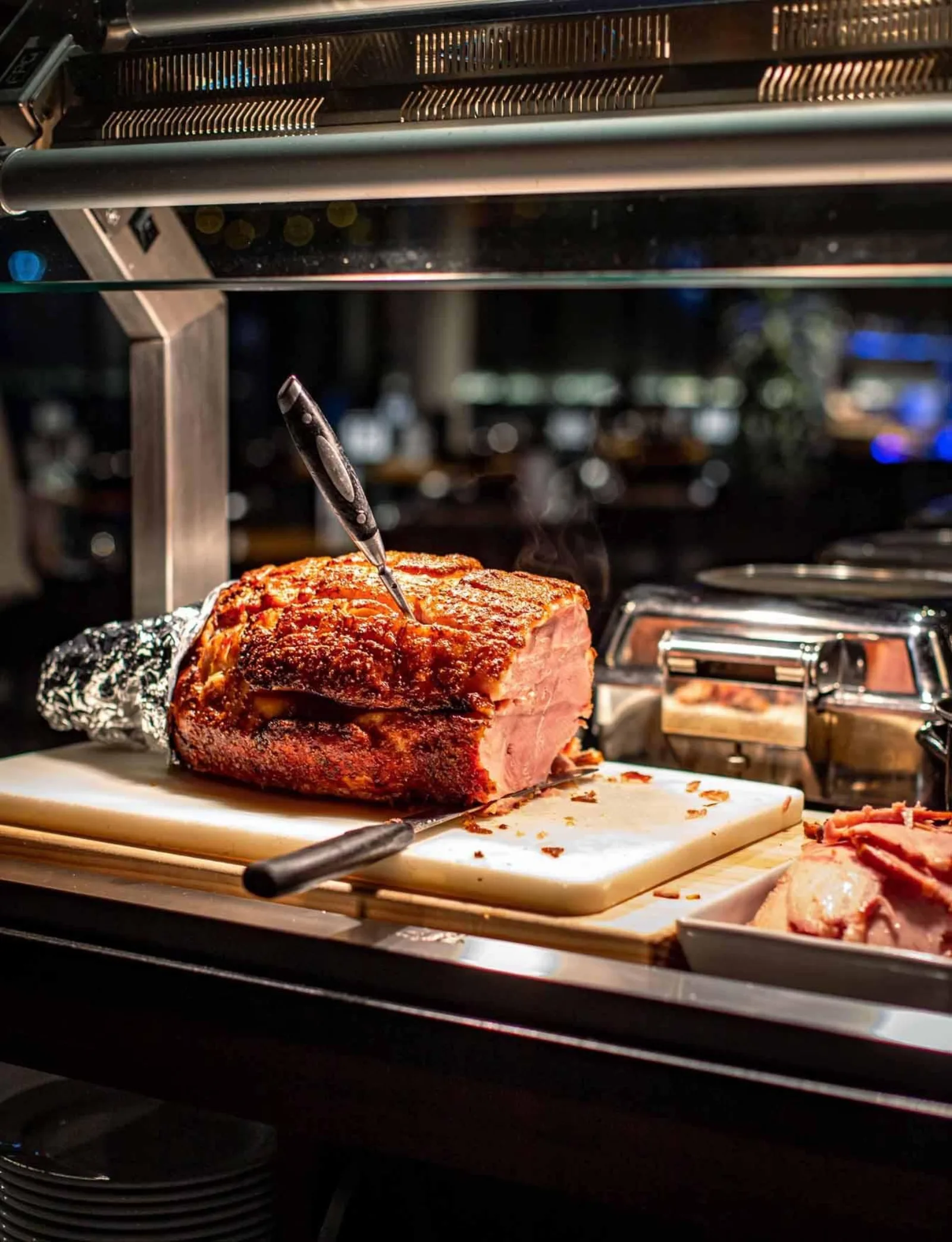 A scored roast pork joint being carved under a heat lamp at the Te Puia carvery