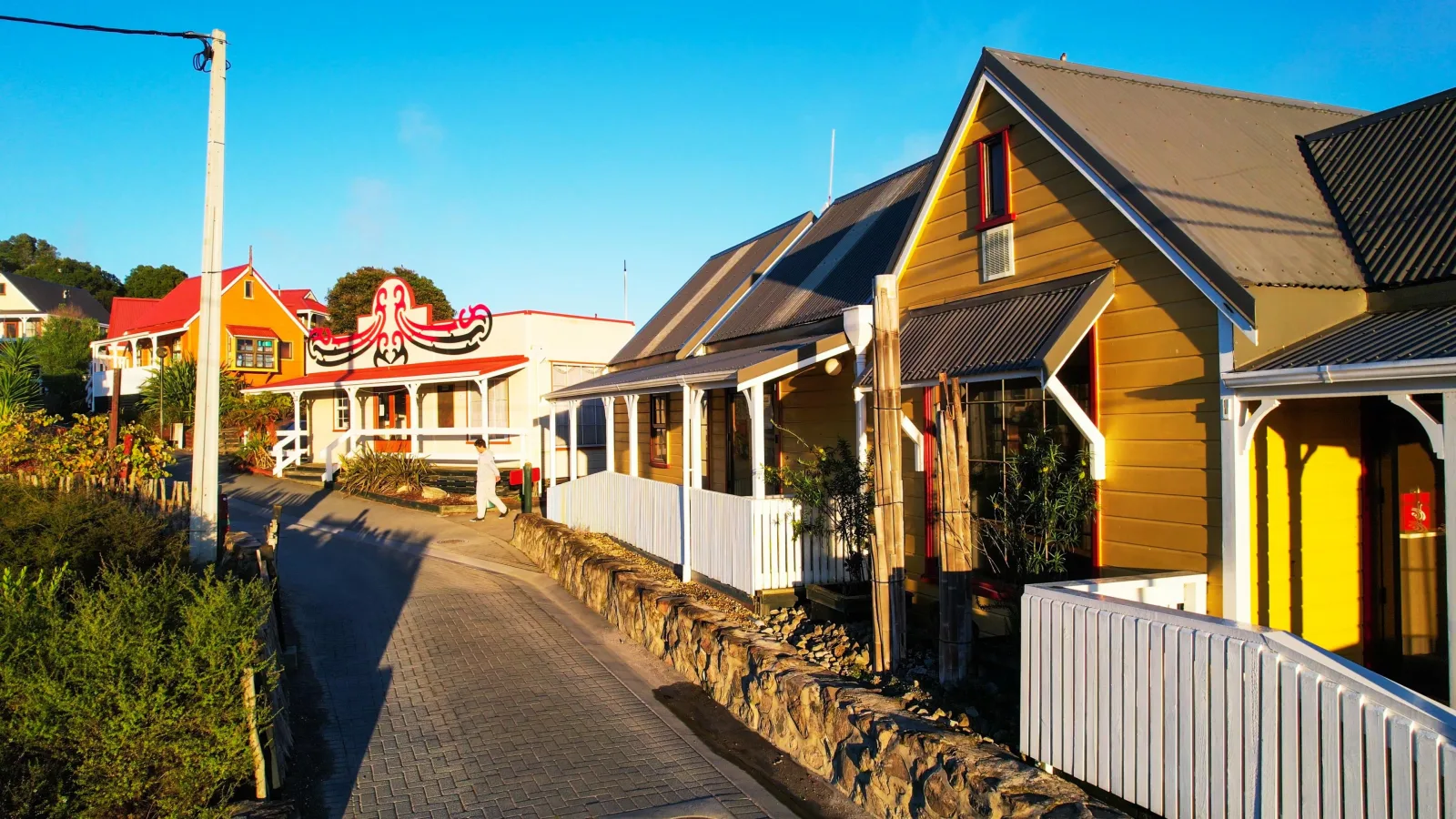 A street inside Whakarewarewa village — weatherboard houses with a red carved gable and steam drifting between them