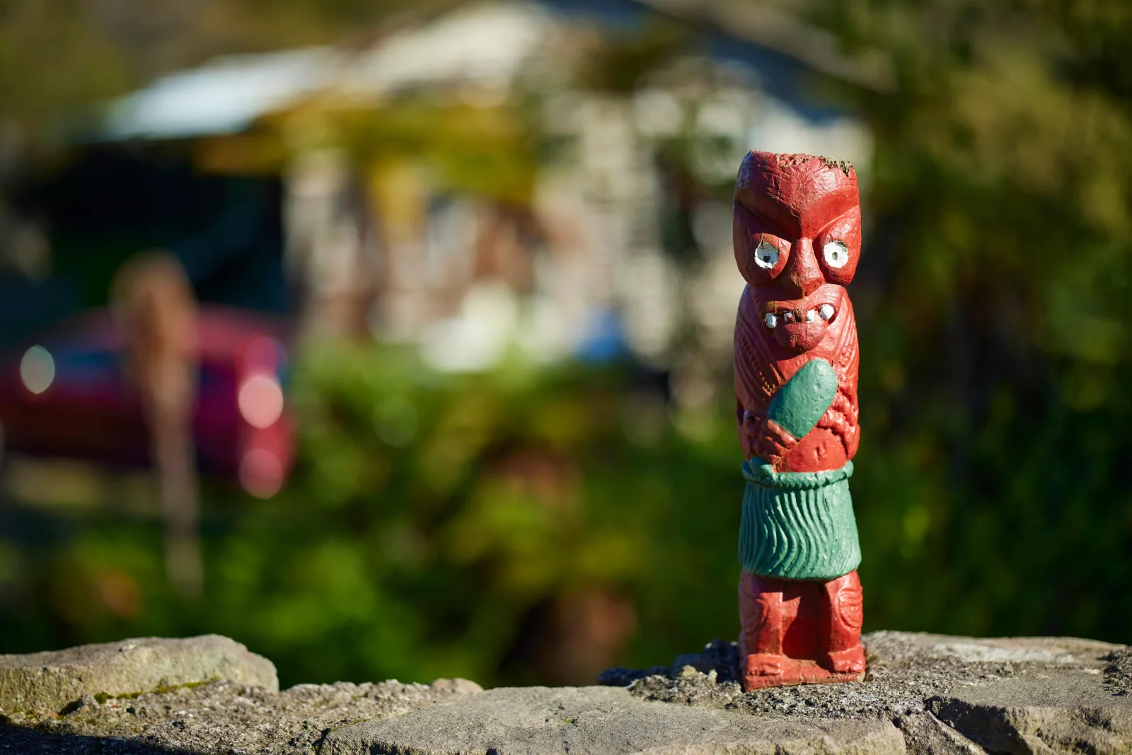 Small painted carved figure on a rock in Whakarewarewa village, houses out of focus behind