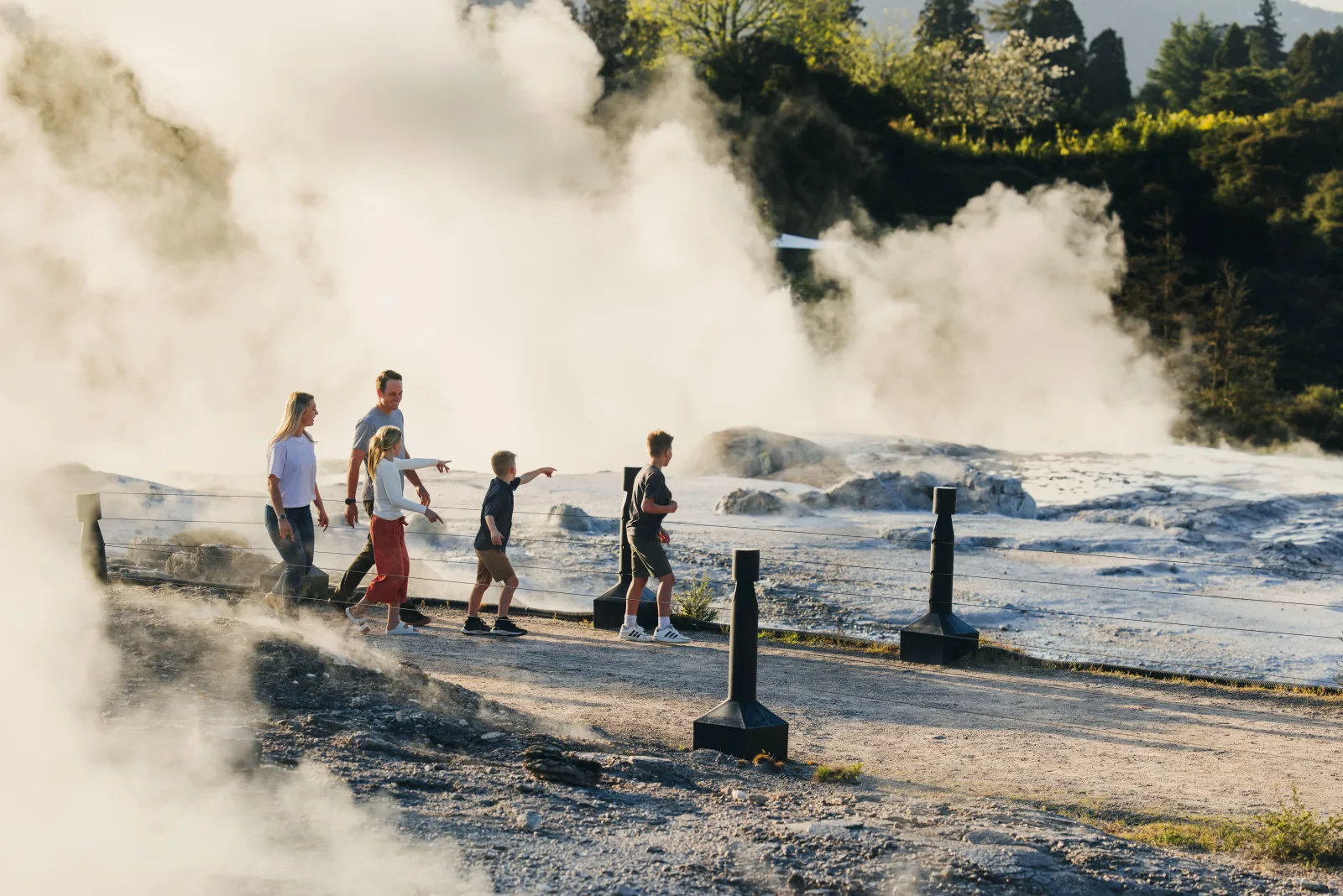 A family walking the boardwalk across the Te Whakarewarewa thermal flat through drifting steam