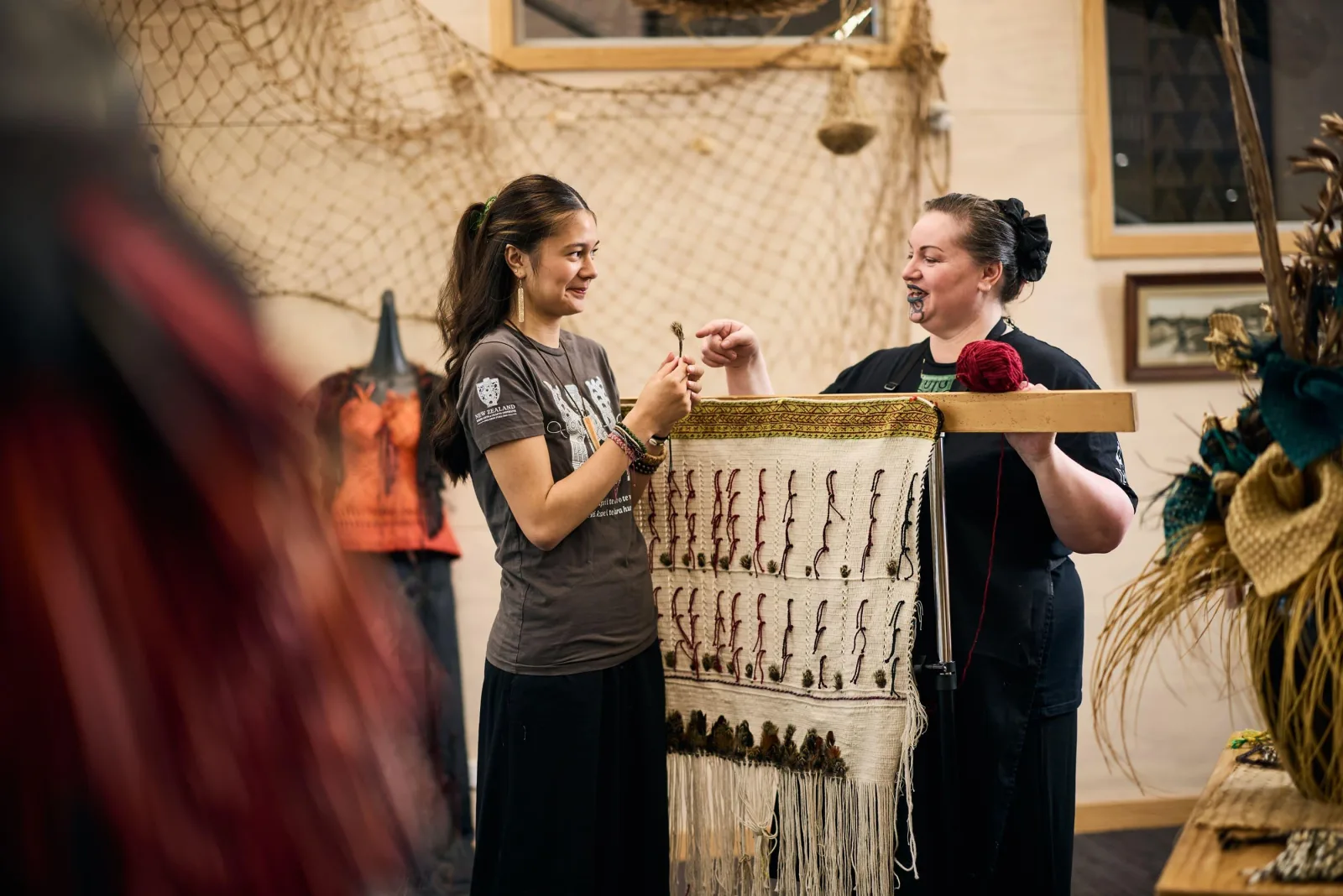 Two weavers at the New Zealand Māori Arts and Crafts Institute working a cloak on an upright frame