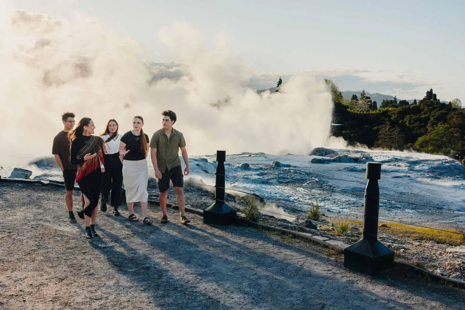A Te Puia guide walking visitors along the silica flat as Pōhutu Geyser erupts behind them
